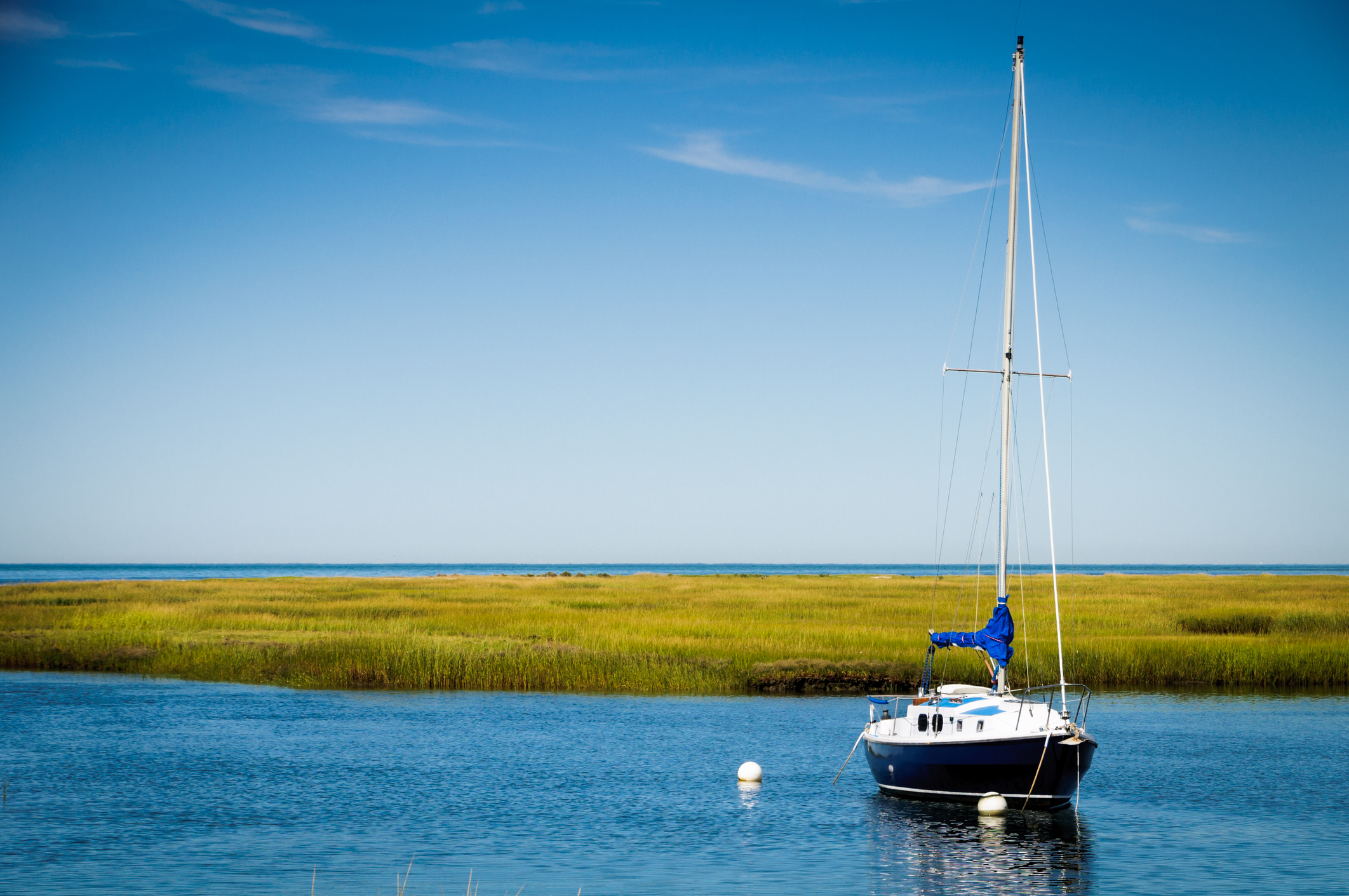 A sleek blue and white sailboat is moored in a quiet inlet of Cape Cod Bay